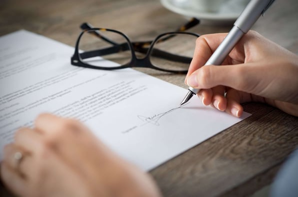 person signing a contract by hand with spectacles on the table